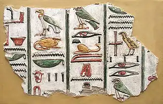 A stone fragment with brightly painted colors and raised-relief images of Egyptian hieroglyphs, written in vertical columns, set against a beige background