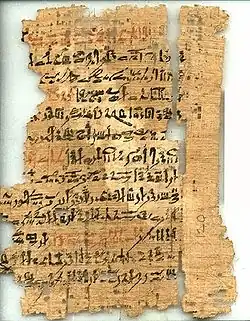 An ancient, torn and fragmented papyrus document, with cursive hieratic handwriting in black and red ink on its surface