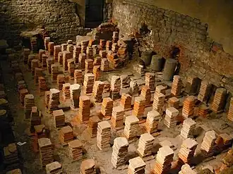 Caldarium. The room uses Roman hypocausts; a floor would have been supported by these structures, where hot air would circulate beneath and heat the room.