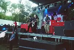 Several men performing onstage, playing instruments and singing into microphones